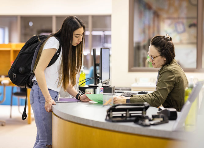 Student talking to librarian behind counter.