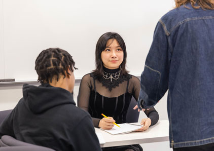 Student listening to a professor at a desk.