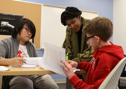 Professor leans in to help students with paper